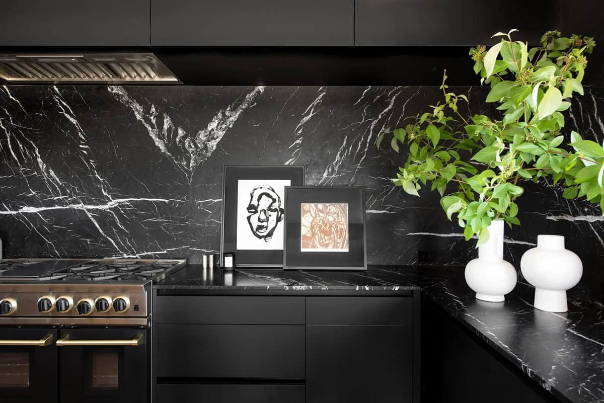 Close-up of black marble kitchen backsplash with professional range, framed artwork, and white ceramic vases