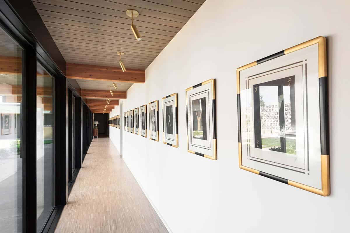 Long hallway with wood plank ceiling, black-framed sliding doors, and gallery wall of gold-framed artwork