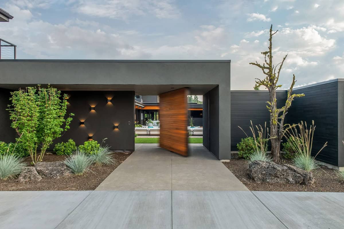 Modern home entry with dark stucco exterior, large pivoting wood door, and desert landscaping