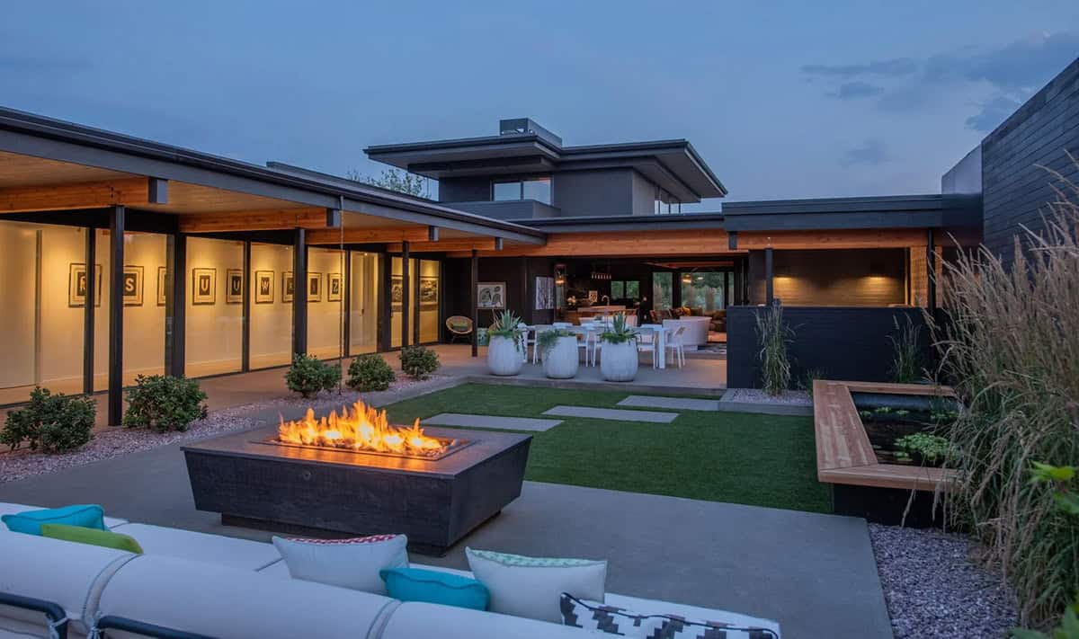 Courtyard at dusk with square fire pit, outdoor sectional seating, white dining set, and illuminated gallery wall
