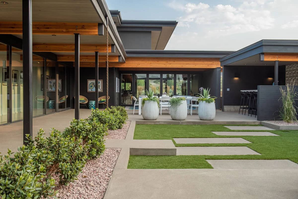 Interior courtyard with concrete stepping stones, turf lawn, large white planters, and covered outdoor dining area
