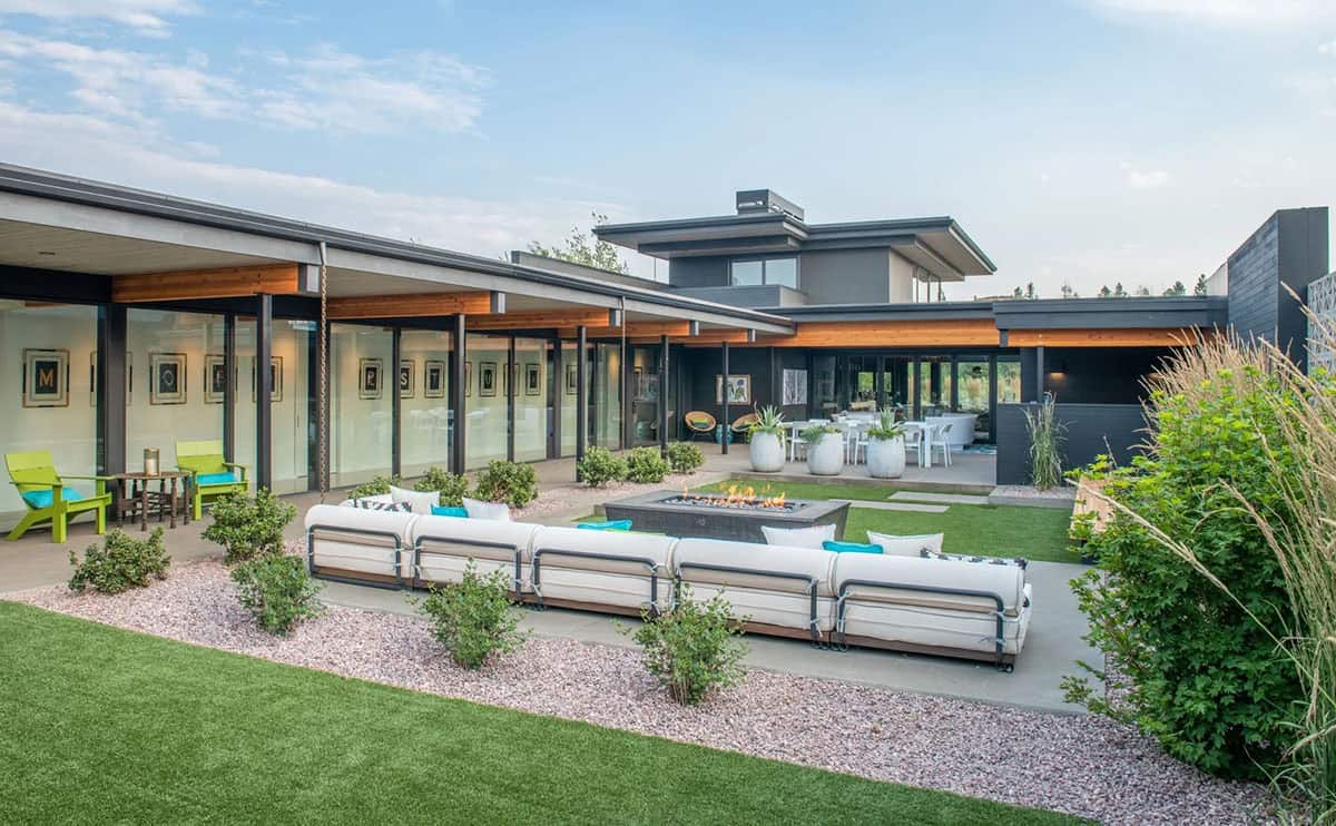 Backyard with U-shaped outdoor sofa around fire pit, lime green accent chairs, gallery corridor, and multi-level roofline