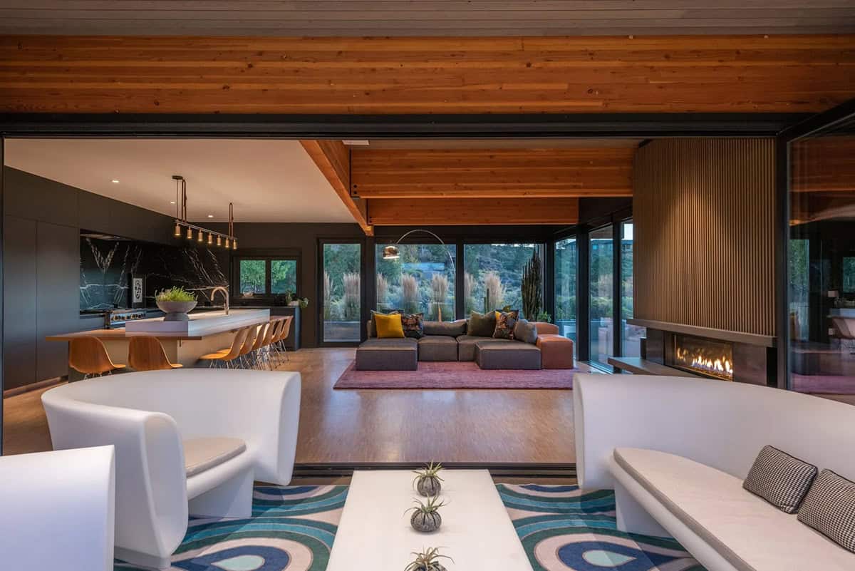 Spacious open-plan interior with white curved seating, sectional sofa, kitchen island, wood beam ceiling, and desert landscape views