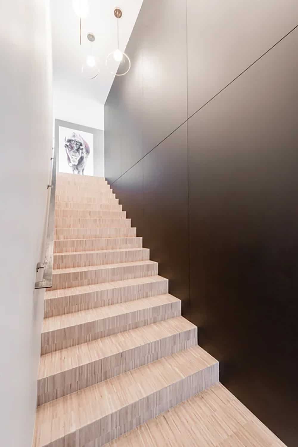 Light wood staircase with dark panel wall, globe pendant lights, and framed bison portrait at the top landing