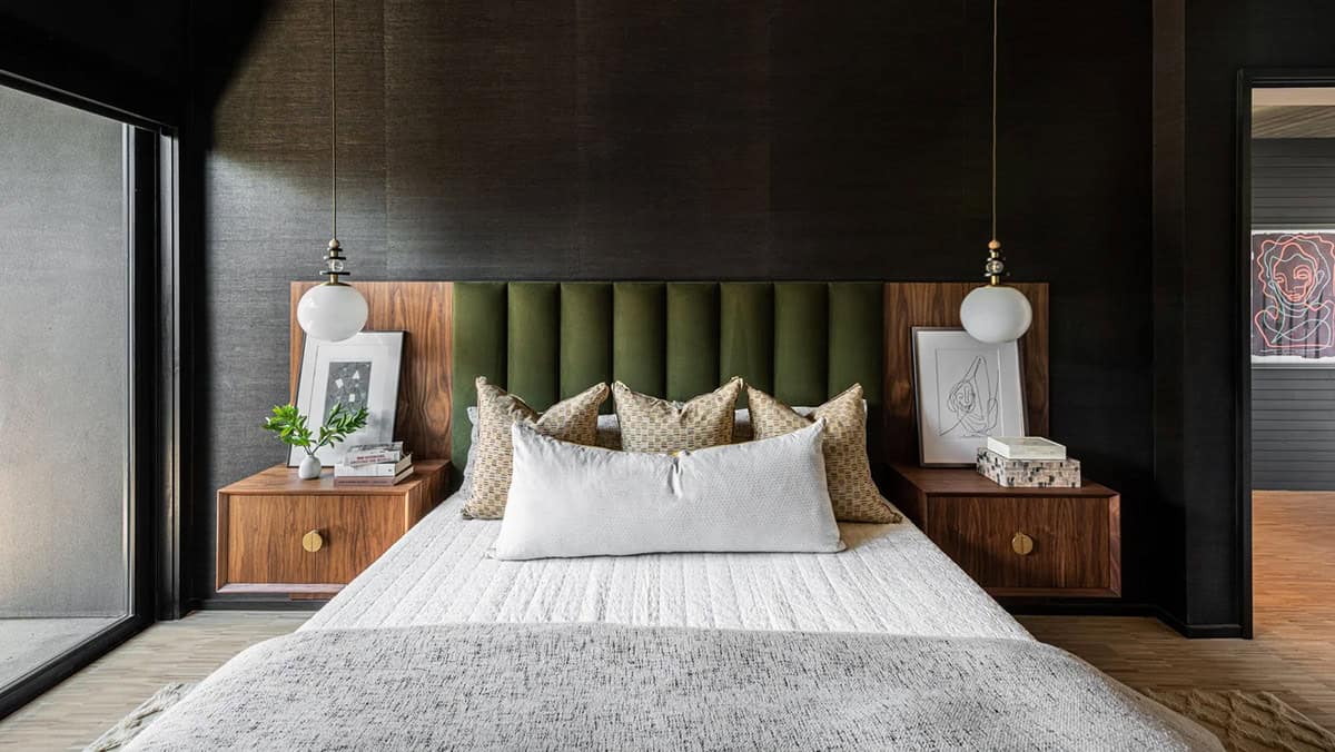 Primary bedroom with dark grasscloth walls, channeled green velvet headboard, walnut nightstands, and globe pendant lights