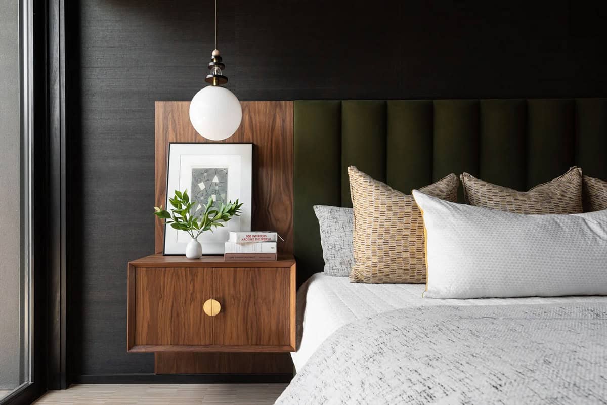Close-up of walnut floating nightstand with brass hardware, globe pendant, framed artwork, and green velvet headboard