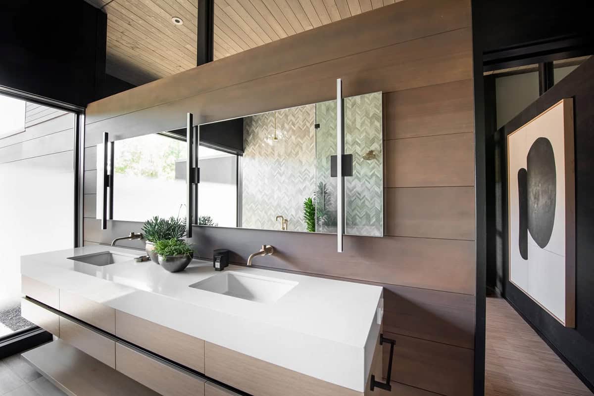 Primary bathroom with floating double vanity, wood plank ceiling, herringbone tile shower, wood-clad accent wall, and brass fixtures