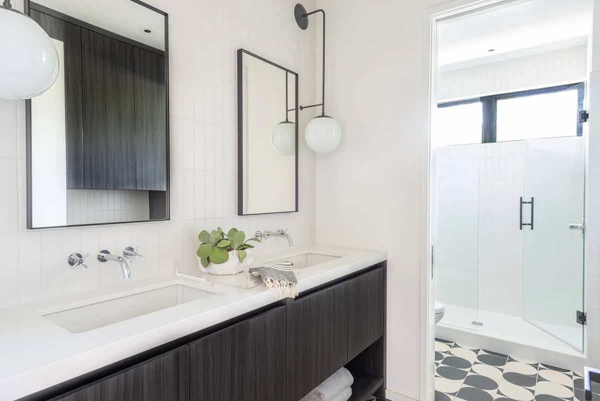 Modern bathroom with dark floating vanity, dual mirrors, globe sconce, white tile walls, and patterned floor tile in shower