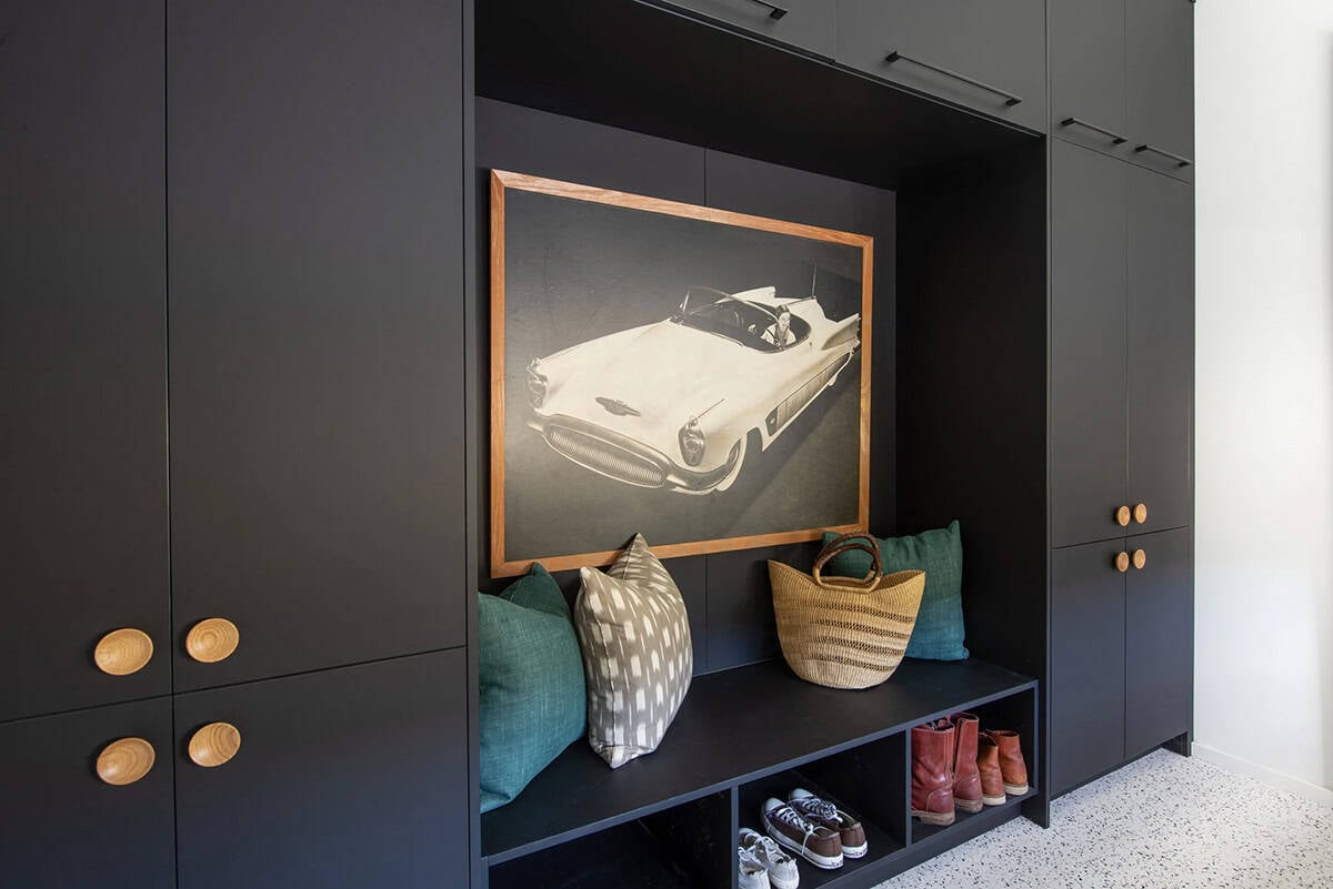 Built-in matte black mudroom with wood knob hardware, bench seating with shoe storage, and framed vintage car photograph