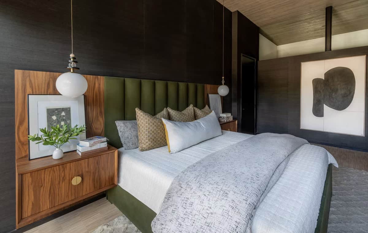 Primary bedroom with dark grasscloth walls, green velvet headboard, walnut nightstands, globe pendants, and large abstract artwork