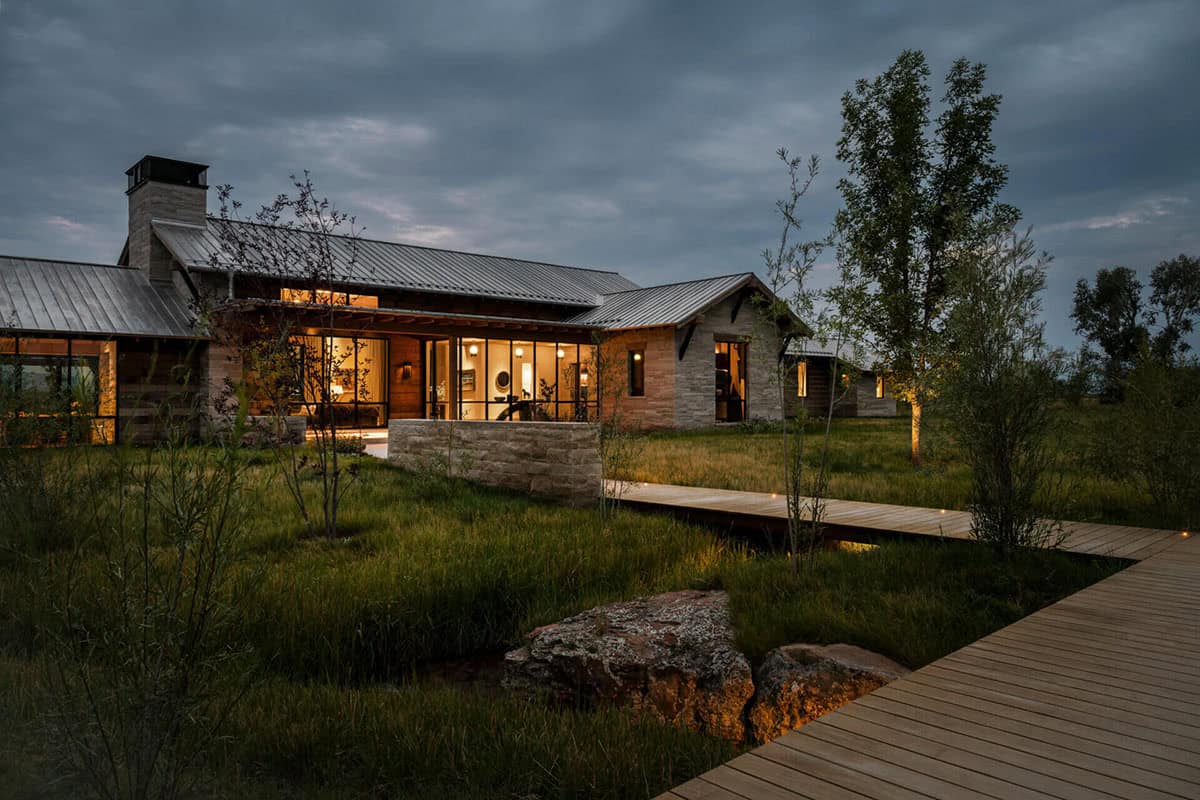Illuminated modern ranch house exterior at night with wooden boardwalk and native grasses