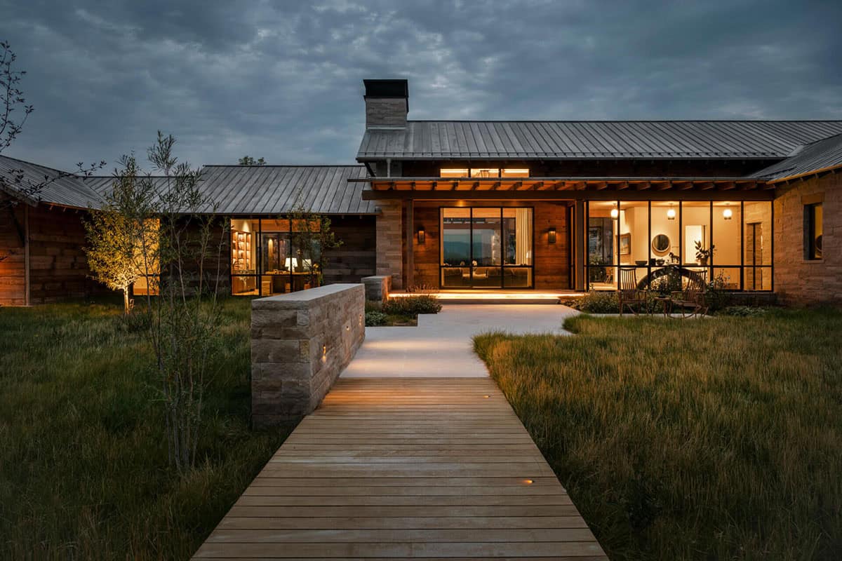 Front entry of a modern ranch house at dusk with lit boardwalk path and steel-framed windows