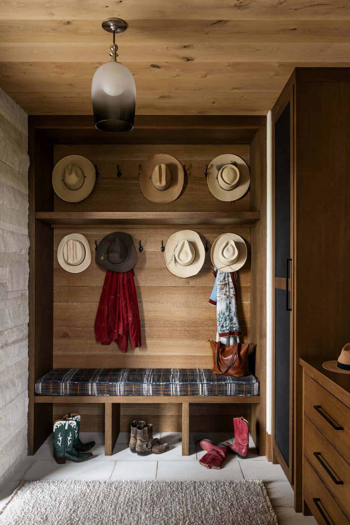 Built-in mudroom with oak cabinetry, cowboy hats, plaid bench cushion, and cowboy boots