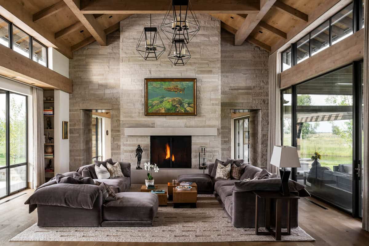 Vaulted great room with stone fireplace, exposed timber beams, geometric pendant lights, and gray sectional sofas