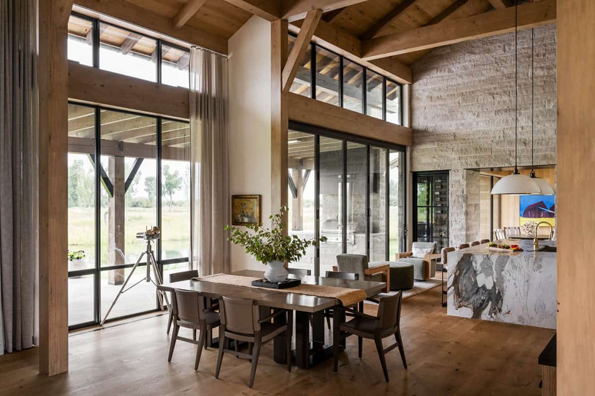Open-plan dining area with dark wood table, floor-to-ceiling windows, and marble kitchen island beyond