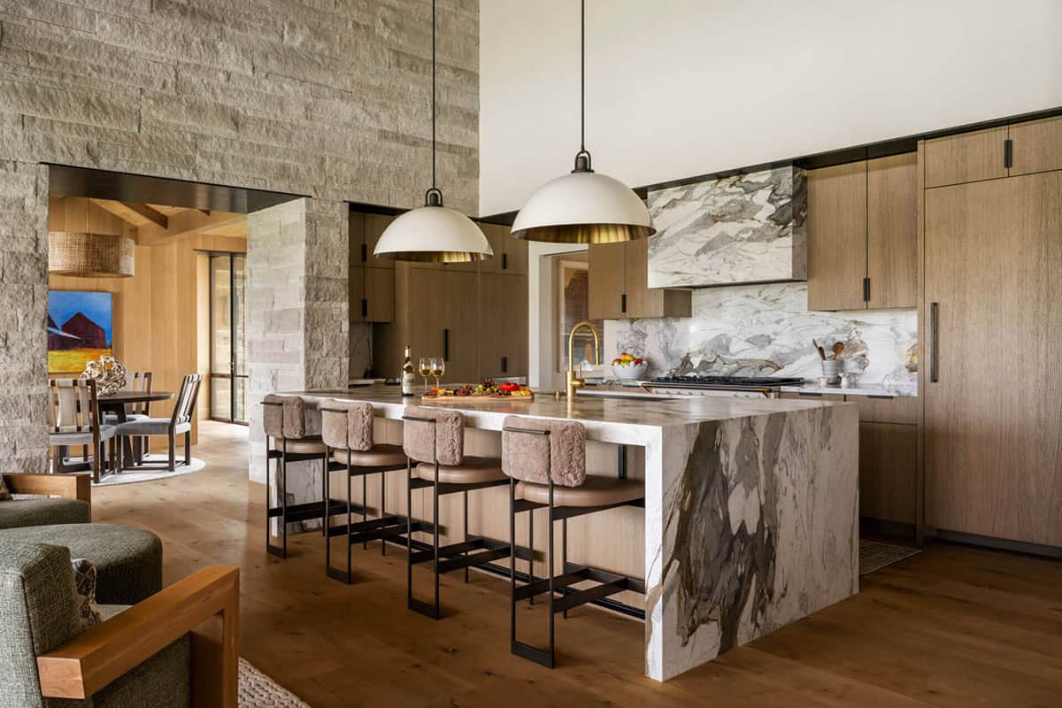 Kitchen with dramatic marble waterfall island, dome pendants, oak cabinetry, and stone backsplash