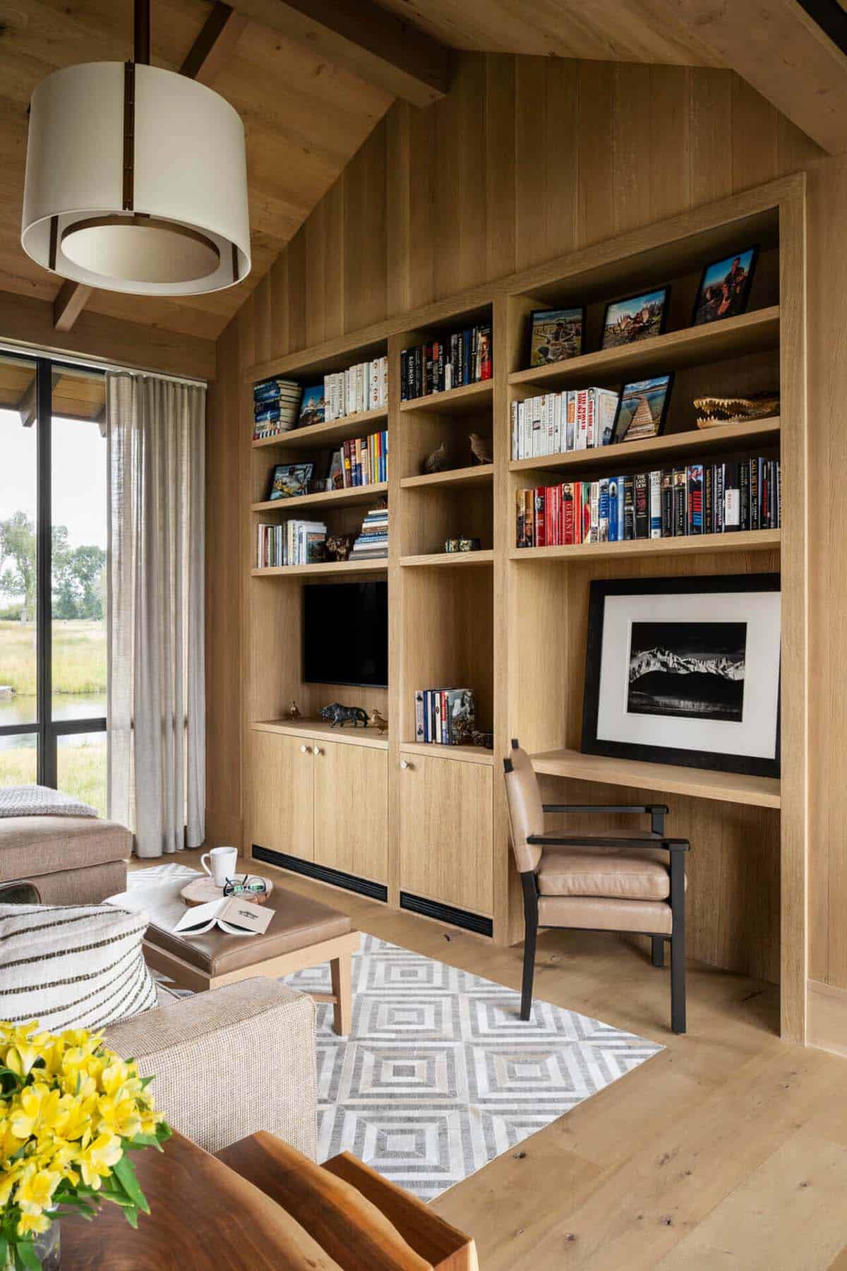 Built-in oak bookcase with integrated TV nook and leather desk chair in a wood-paneled den