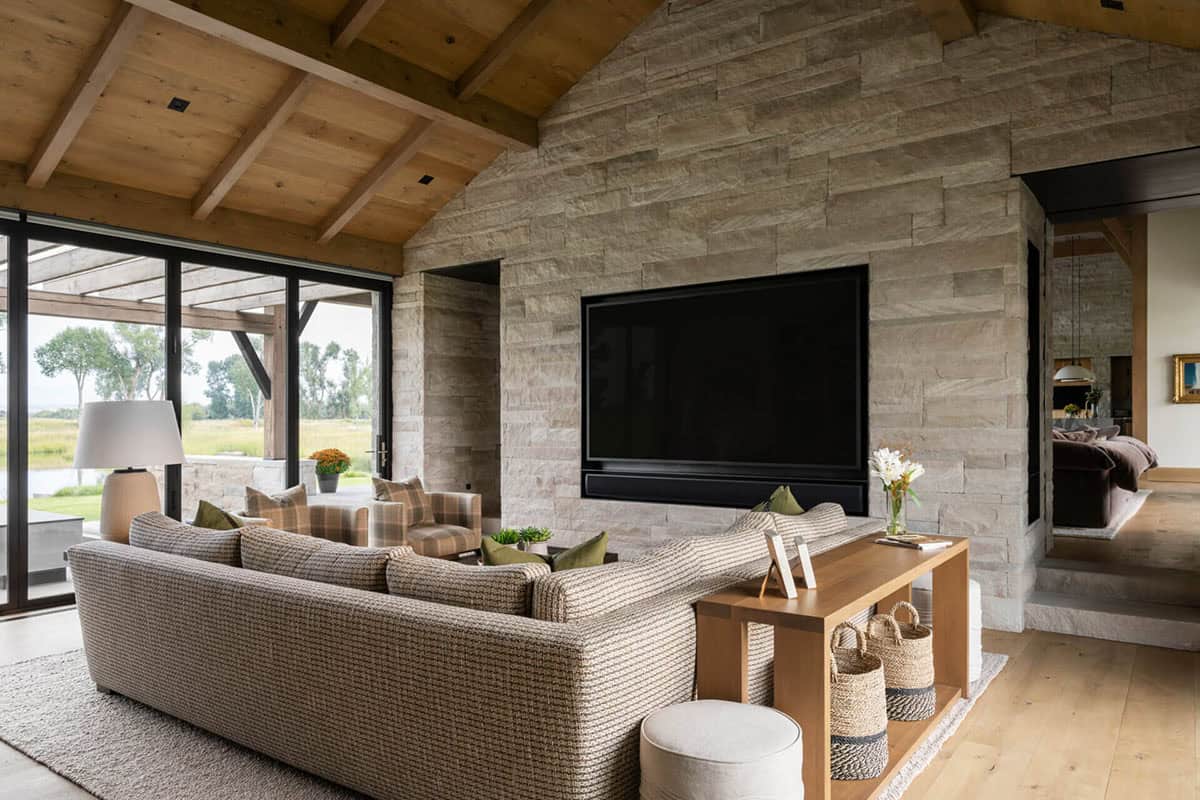 Family room with stone TV wall, textured sectional sofa, plaid armchairs, and sliding glass doors to the outdoors