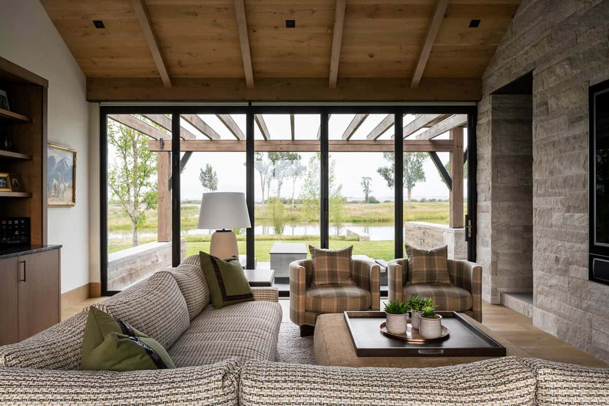 Casual sitting room with woven sectional, plaid club chairs, and floor-to-ceiling windows overlooking a Montana pond