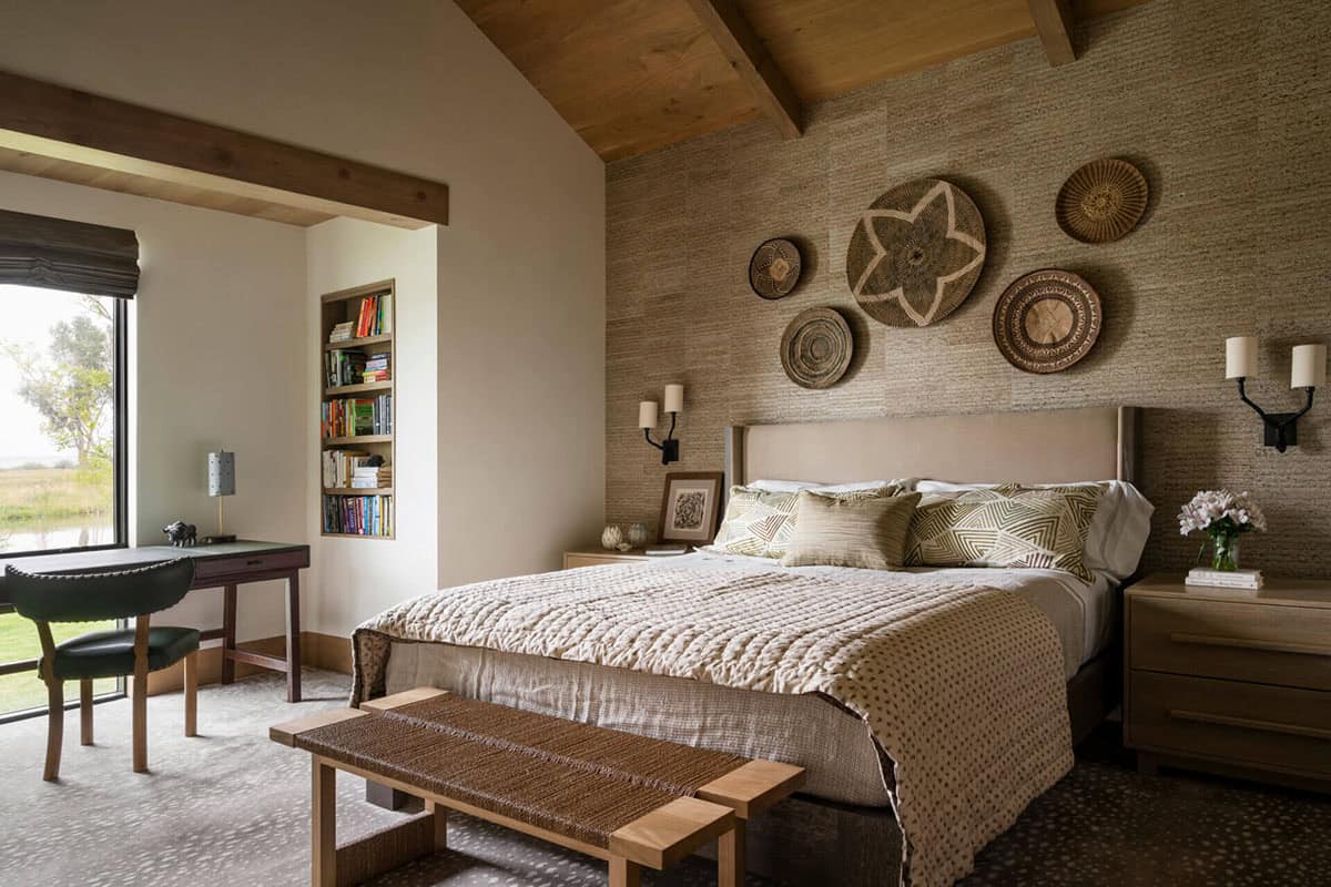 Guest bedroom with grasscloth accent wall, woven basket wall art, upholstered headboard, and built-in bookcase nook