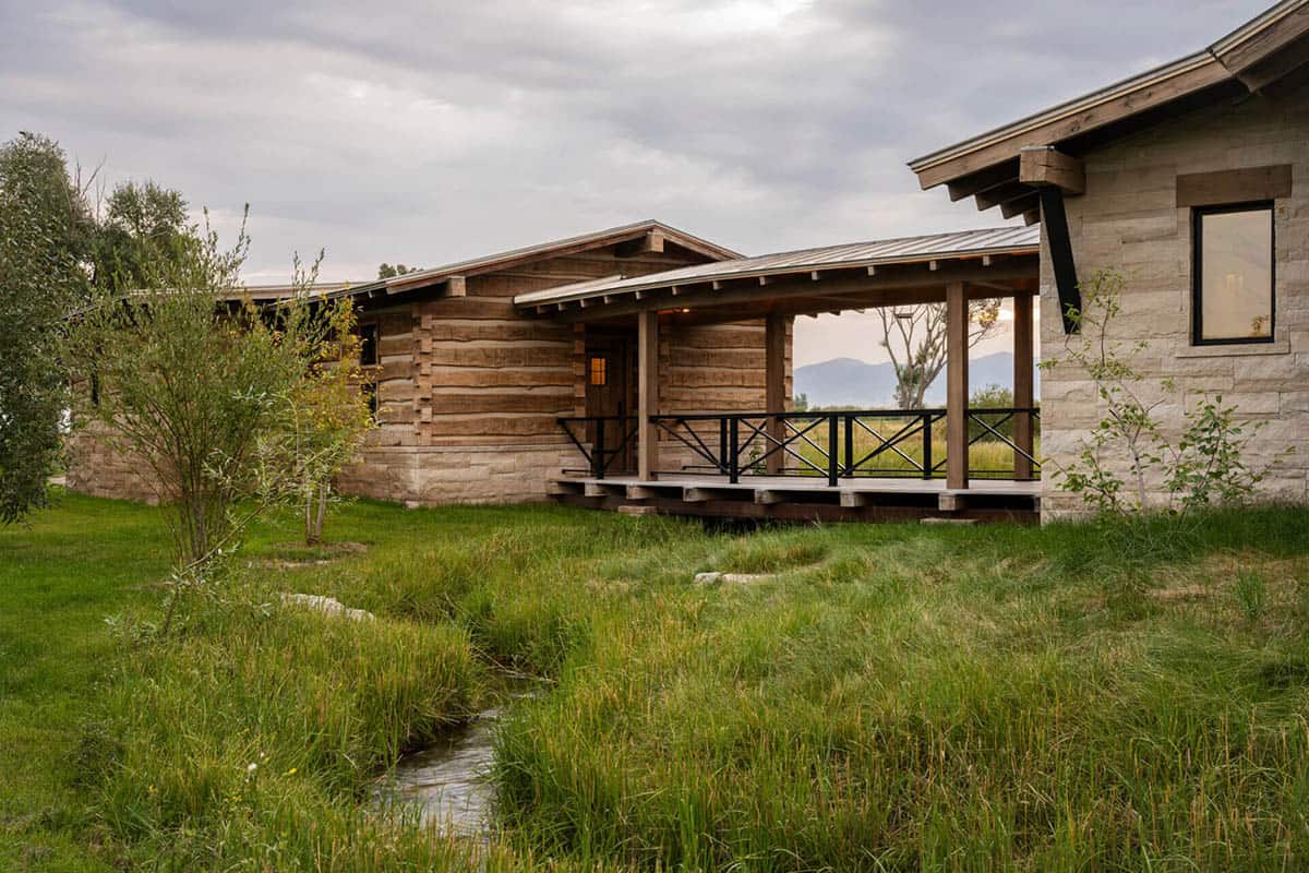 Reclaimed log cabin guest wing exterior with covered porch and mountain views beyond native grasses