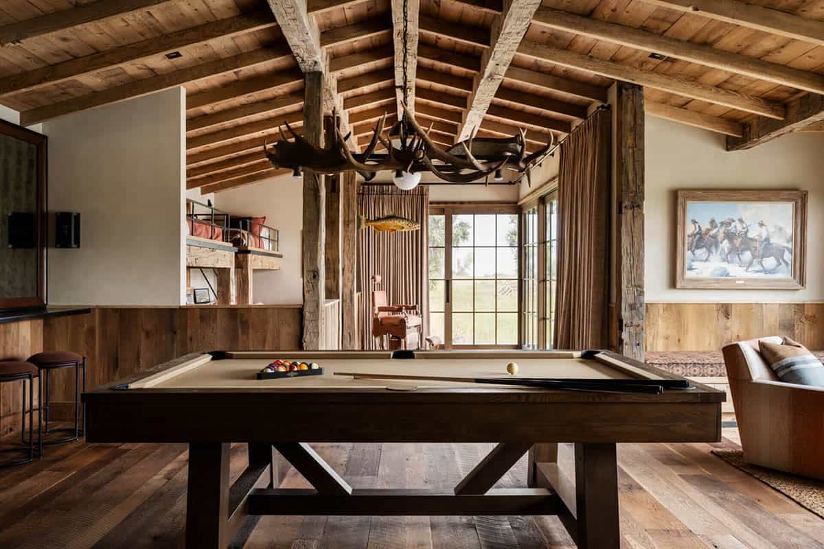 Game room with pool table, antler chandelier, reclaimed wood ceiling, and Western painting on paneled walls