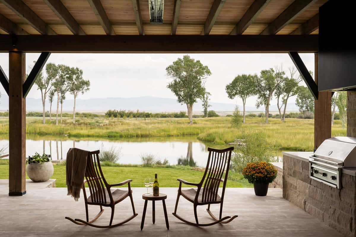 Covered porch with two rocking chairs overlooking a pond and Montana grasslands with mountain views