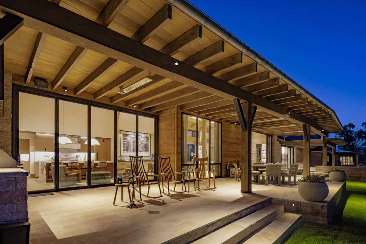Illuminated back patio at night with rocking chairs, timber pergola, and open views into the kitchen and dining areas