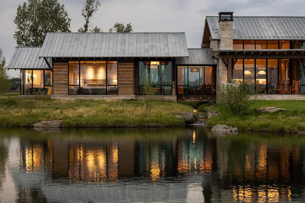 Modern ranch house wings glowing at dusk, reflected in a still pond with a small waterfall feature
