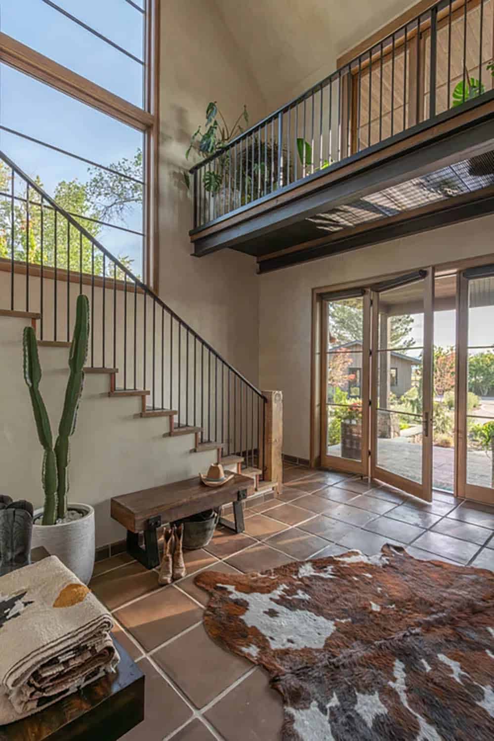 Two-story foyer with steep staircase, terracotta tile floor, and cowhide rug
