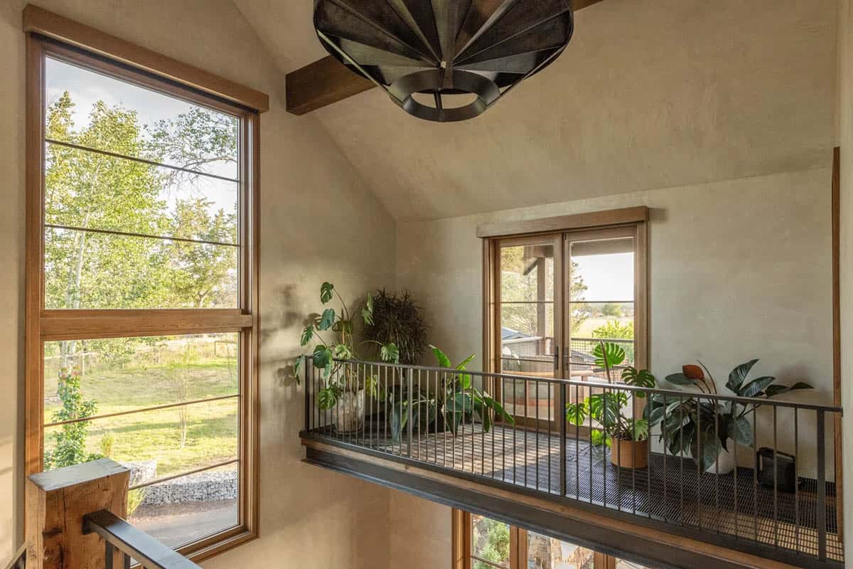 Open loft hallway with plants along iron railing and tall windows