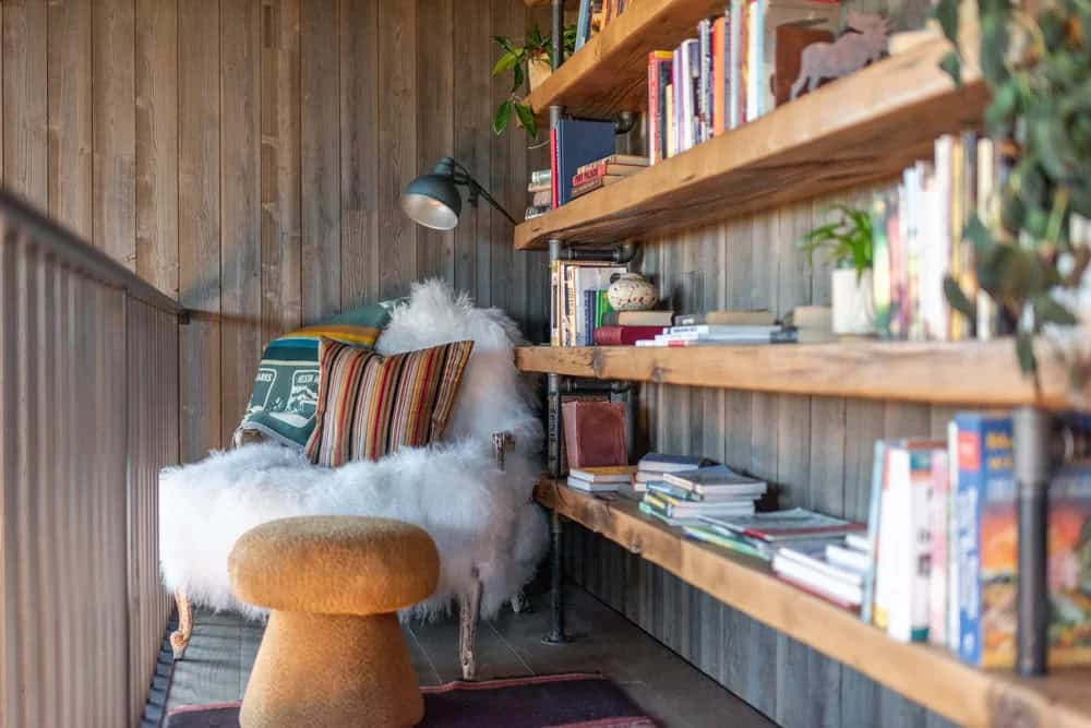 Cozy reading nook with sheepskin chair and rustic pipe bookshelves