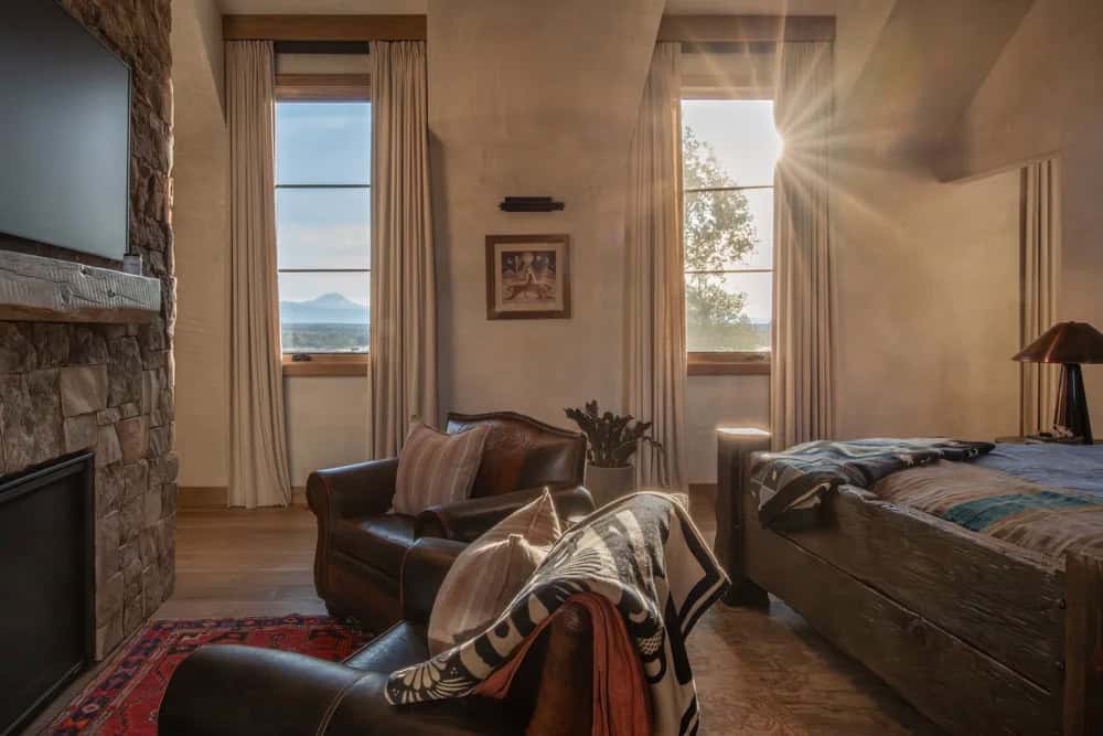 Bedroom with leather armchairs, stone fireplace, and mountain view