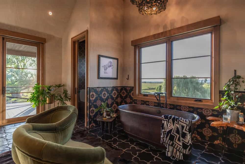 Bathroom with copper soaking tub, patterned tile, and green velvet chairs