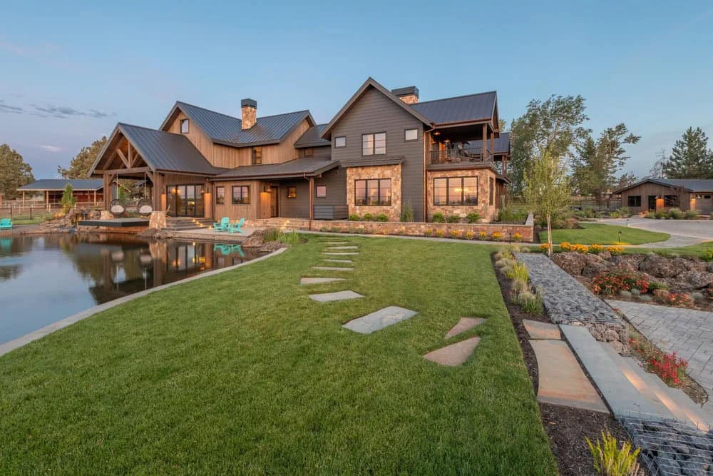 Rear exterior of ranch house with stone accents overlooking pond and lawn