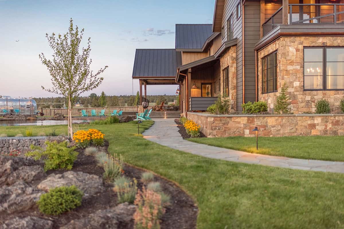 Side exterior view of stone and wood house with landscaped path at sunset