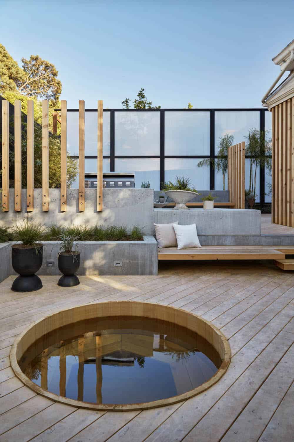A round cedar soaking tub sunk into a cedar deck with modern Shoji-inspired wood screens and a translucent fence