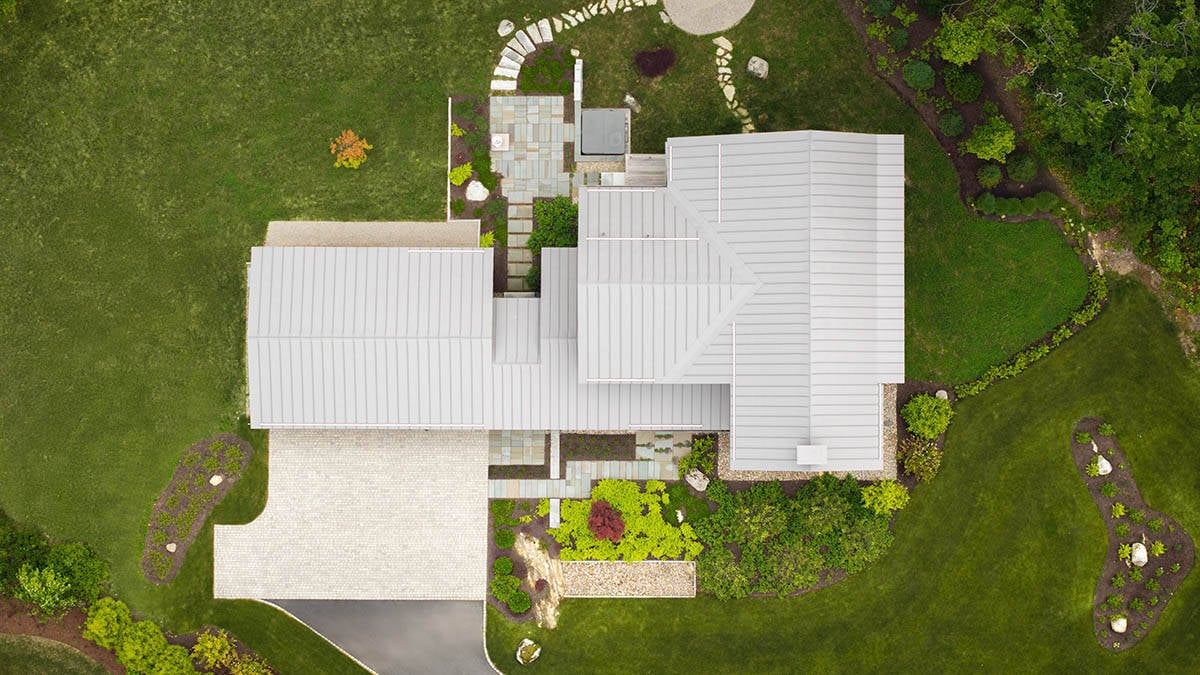 Overhead drone view of T-shaped metal roof home with landscaped grounds in Kennebunkport, Maine