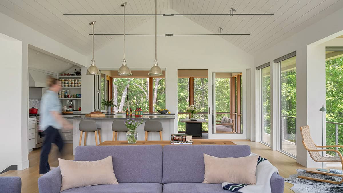 Open-plan living and kitchen area with vaulted ceiling, forest views, and screened porch beyond