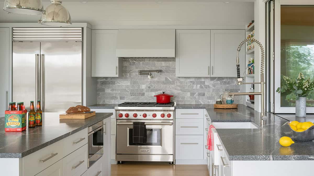 White kitchen with Wolf range, marble tile backsplash, and stainless steel appliances
