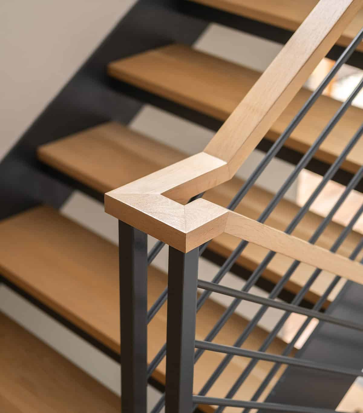 Close-up of sculptural steel staircase railing with warm oak treads and open risers