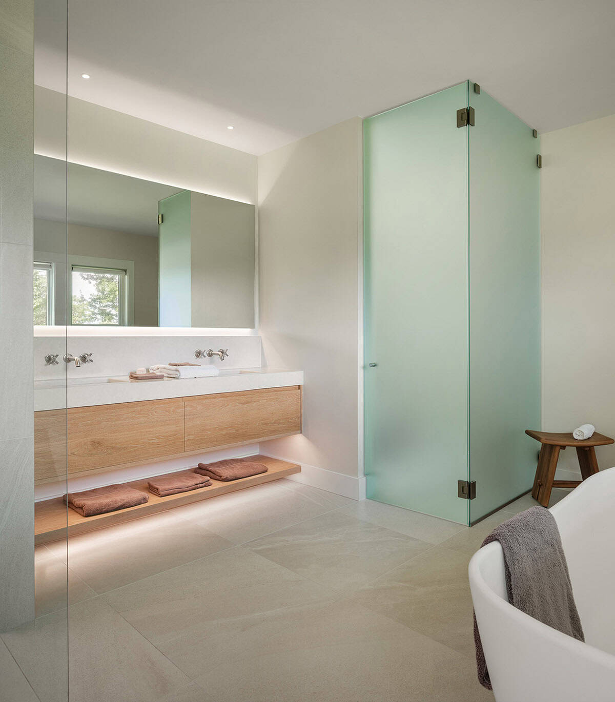 Primary bathroom with floating oak vanity, backlit mirror, frosted glass shower enclosure, and soaking tub
