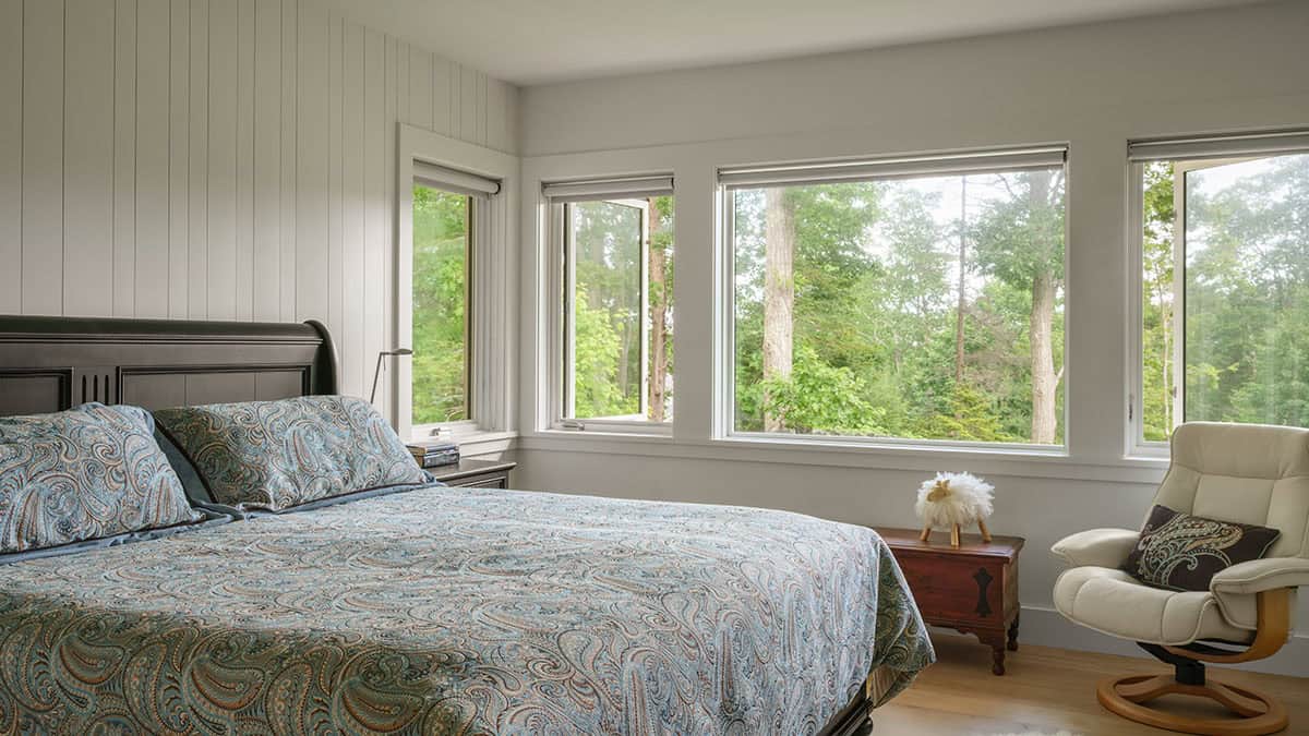 Primary bedroom with shiplap walls, forest views through low-sill windows, and hardwood floors