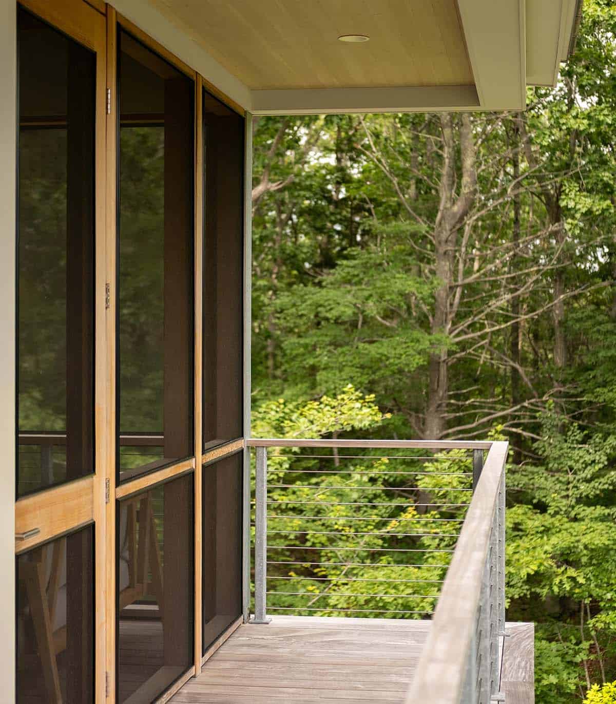 Screened porch exterior with cedar-framed screens, wood-ceiling soffit, and cable railing overlooking woods