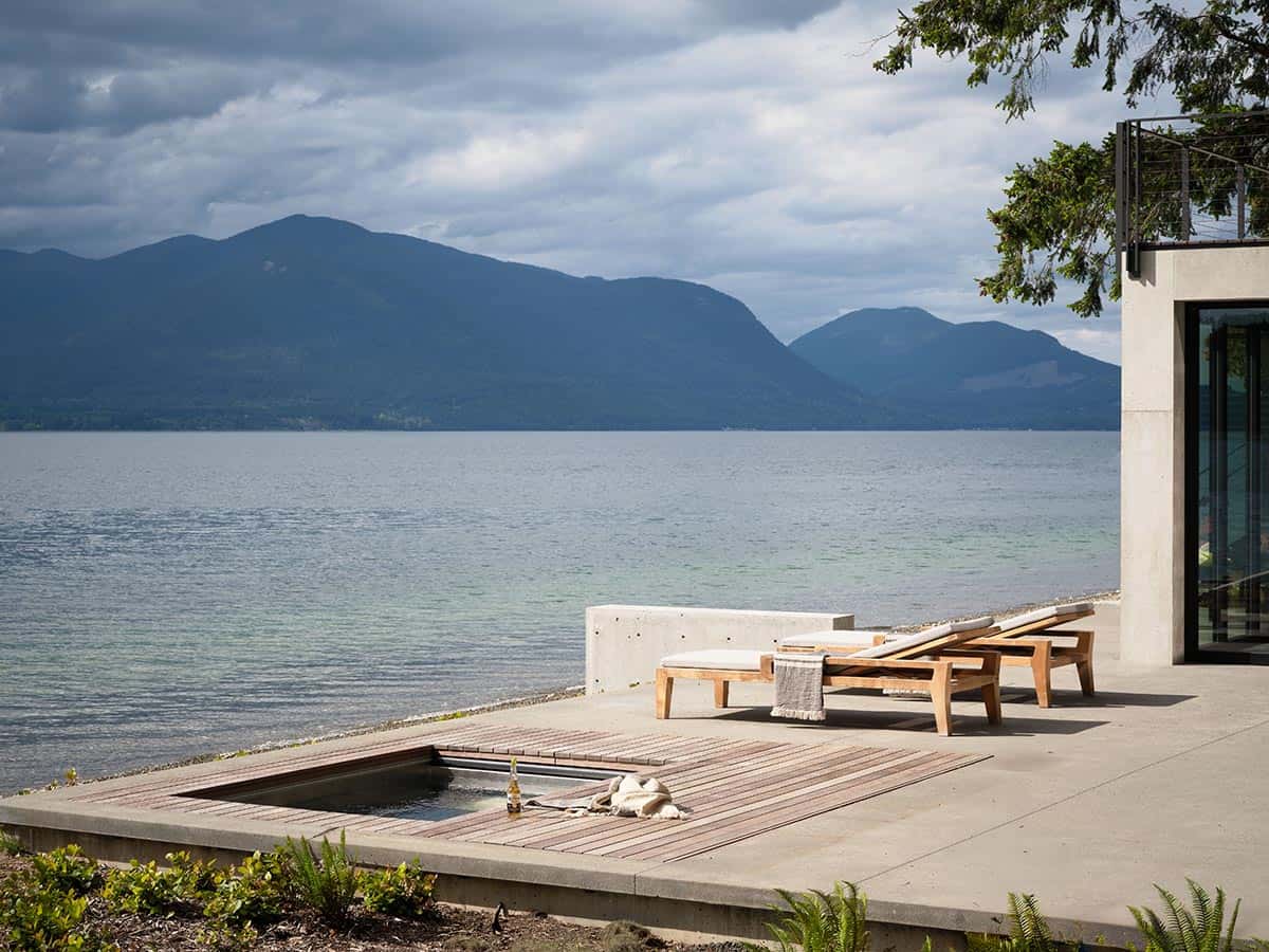 Concrete waterfront terrace with teak lounge chairs and flush plunge pool facing mountain lake