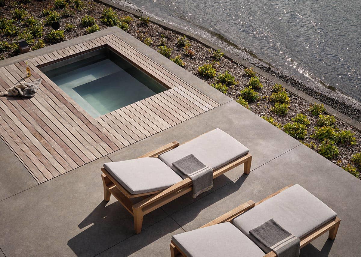 Aerial view of teak-decked plunge pool on concrete terrace beside a rocky shoreline
