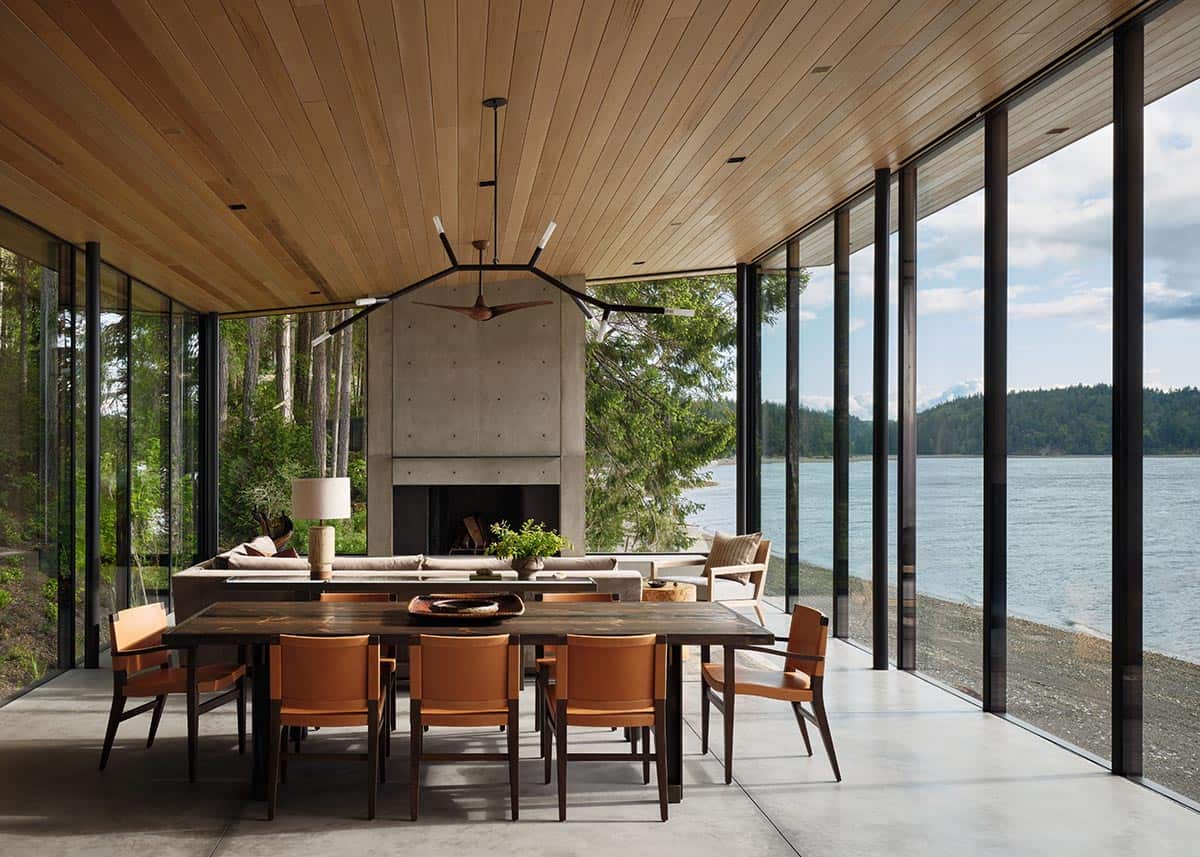 Open-plan dining and living area with cedar ceiling, concrete fireplace, and panoramic water views
