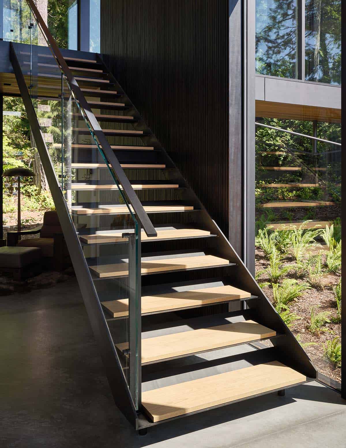 Floating oak stair treads on steel stringer with glass balustrade beside forest-view windows