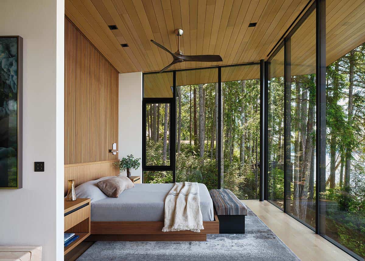 Primary bedroom with wood slat accent wall, cedar ceiling, and floor-to-ceiling forest views