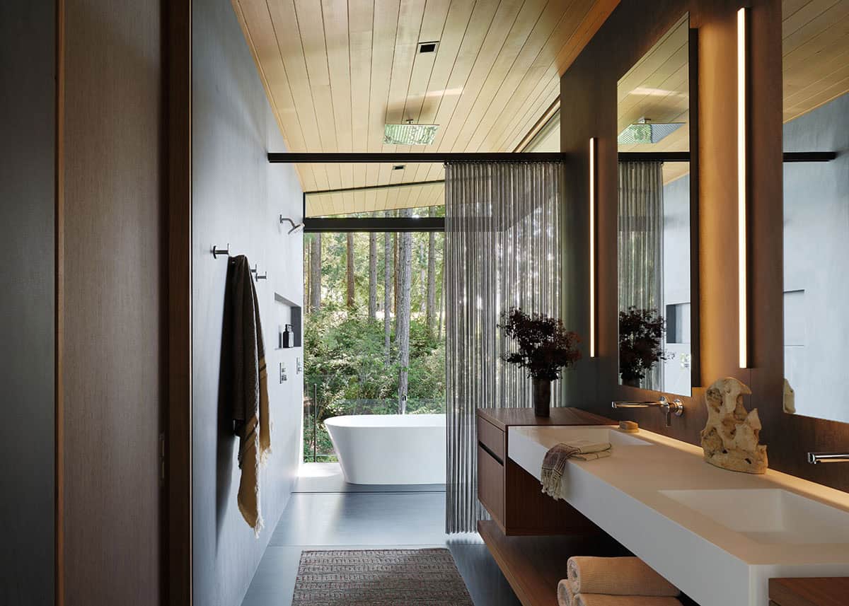 Spa bathroom with wood ceiling, freestanding tub, and sheer curtain beside forest-view glazing
